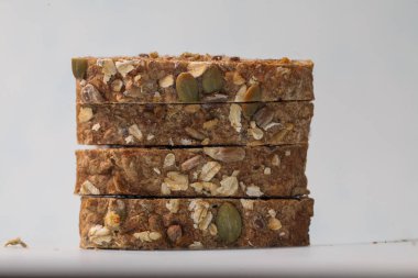 Fındık ve çekirdekli lezzetli granola çubukları temiz beyaz bir yüzeye güzelce istiflenmiştir. Yumuşak, doğal ışıkla aydınlatılır. Besleyici bir atıştırmalık için mükemmeldir..