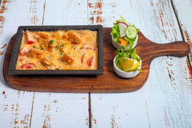 Canlı bir yemek, taze bir sebze salatasıyla birlikte sıcak, siyah bir tabakta servis edilen, zengin bir sosta pişirilmiş taze bir tavuğu içerir..