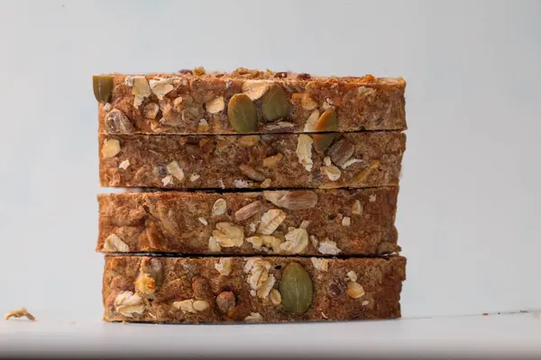 Fındık ve çekirdekli lezzetli granola çubukları temiz beyaz bir yüzeye güzelce istiflenmiştir. Yumuşak, doğal ışıkla aydınlatılır. Besleyici bir atıştırmalık için mükemmeldir..