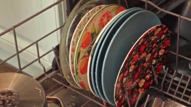 Renkli tabaklar bir bulaşık makinesinde düzgünce istiflenir, çeşitli çiçek ve meyve tasarımları sergilenir. Bu, yemekten sonra mutfak aletlerinin düzenlenmesini ön plana çıkarır.