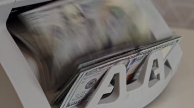 Bir nakit sayma makinesi yeni istiflenmiş banknotları hızla işleyerek hareket bulanıklığı yaratır. Ayarlar, paranın sıklıkla kullanıldığı hareketli bir ofis atmosferini gösteriyor..
