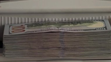 Düzgünce düzenlenmiş yüz dolarlık banknotlar para sayma makinesinde duruyor. Bu da para işleme veya bankacılık ile ilgili aktiviteleri gösteriyor..