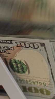 Yüz dolarlık banknotun yakın plan bir kasanın içindeki bir yüzeyde durması tasarımın ve güvenlik özelliklerinin karmaşıklığını yansıtıyor. Dikey video.