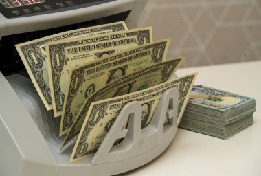 A currency counting machine is sorting multiple one-dollar bills while a stack of neatly organized banknotes is placed beside it. clipart