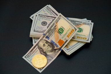 Tanınmış bir Bitcoin 'in yanında yüz dolarlık banknotlar yığını, geleneksel finans ve dijital para birimi arasındaki bağlantıyı şık bir ekranda vurguluyor.