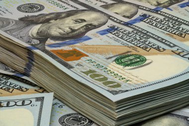 Düzenli bir şekilde yığılmış yüz dolarlık banknotların detaylı bir görüntüsü canlı renklerini ve çalışma alanındaki yumuşak ışıklandırma altında karmaşık tasarımlarını sergiliyor..
