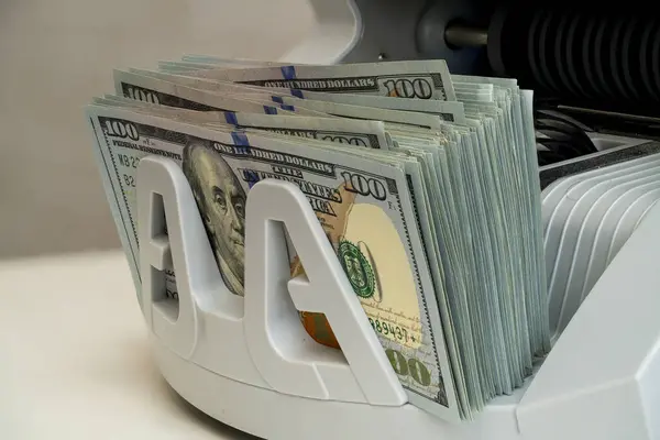Bir para sayma makinesi, 100 dolarlık banknotları bir araya toplar ve finansal ortamda doğru sayıma hazır temiz bir para düzenini gösterir..