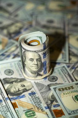 Yuvarlanan yüz dolarlık banknotlar, sayısız yelpazelenmiş banknotların arasında belirgin bir şekilde duruyor. Para bolluğu mali refah ve zenginliği akla getiriyor..