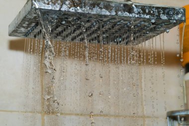 Banyodaki metal bir duş başlığından düşen su damlacıkları rahatlatıcı bir akış oluşturur. Döşeme duvarları, yumuşak ışıkla birleşmiş temiz bir çevreyi yansıtıyor..