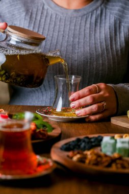 Lezzetli abur cuburlarla çevriliyken bir insan bardağa sıcak çay doldurur. Ortam, rahatlama ve sosyalleşme için mükemmel sıcak bir atmosfere sahip..