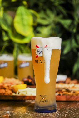 Köpüklü uzun bir bardak hafif bira çeşitli lezzetli aperatiflerin önüne konur. Yeşillik bir zemin görevi görüyor, canlı bir ortam yaratıyor..