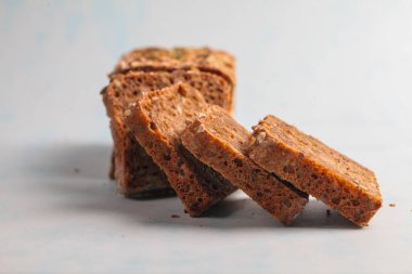 Bir somun tam tahıllı ekmek kalın parçalar halinde dilimlenir, zengin dokusu ve içeriği yumuşak mavi bir zemin üzerinde sergilenir, tazeliği vurgular..