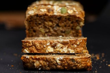 Dilimlenmiş tahıllı ekmek çeşitli tohumlar ve tahıllar sergiliyor. Doku ve renk bu besleyici somunun ev yapımı kalitesini vurgular.