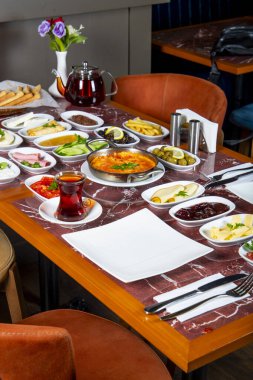 A beautifully arranged table displays an array of traditional breakfast dishes, including cheeses, olives, and vegetables, accompanied by tea and bread. clipart