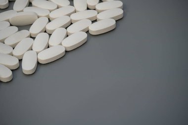 Çeşitli beyaz tabletler gri bir yüzeye dağılmış oval şekillerini ve pürüzsüz dokularını sergiliyorlar. Nötr ışıklandırma ayrıntıları açıkça vurguluyor..