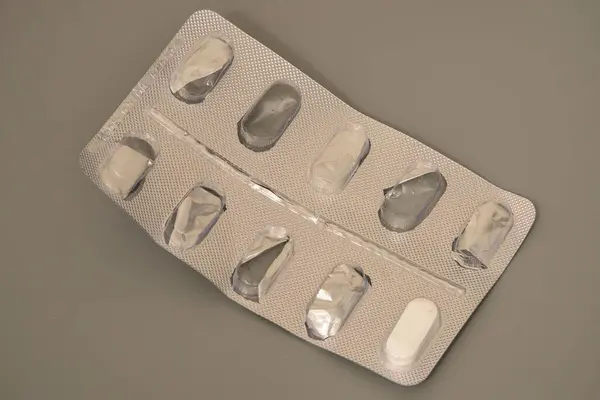 Çeşitli tabletleri içeren bir su toplayıcısı gri bir yüzeyde, birkaç yuvası boş duruyor. Pakette çeşitli tablet şekilleri ve boyutları gösteriliyor..