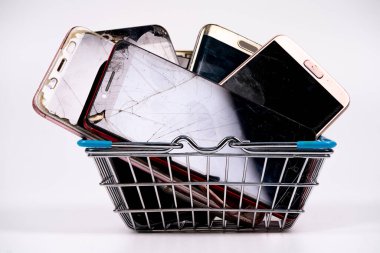 A variety of old and damaged smartphones are piled into a small wire basket, ready for recycling. This collection highlights electronic waste and sustainability. clipart