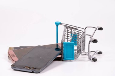 Birkaç eski akıllı telefon, aşınma belirtileri gösteriyor, küçük bir alışveriş arabasının yanında, teknoloji ve tüketiciliğin yan yana dizilmesini sağlıyor..