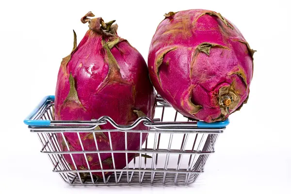 Parlak pembe derili iki canlı ejderha meyvesi küçük bir metal alışveriş sepetine yerleştirilmiştir. Meyvenin eşsiz görünüşü tropikal cazibesini vurgular..