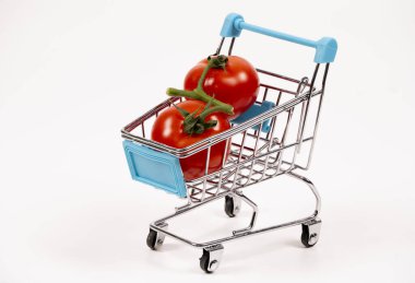 Küçük bir alışveriş arabasında yeşil saplı iki olgun kırmızı domates var. Temiz beyaz bir zemin üzerinde taze bir market eşyası sergileniyor. Yemek pazarlama için ideal..