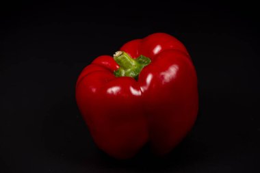Canlı bir kırmızı dolma biber, parlak derisini ve farklı şeklini vurgulayan siyah bir arkaplan karşısında sergilenir. Mutfak kullanımı ya da sanatsal gösterimler için mükemmel.