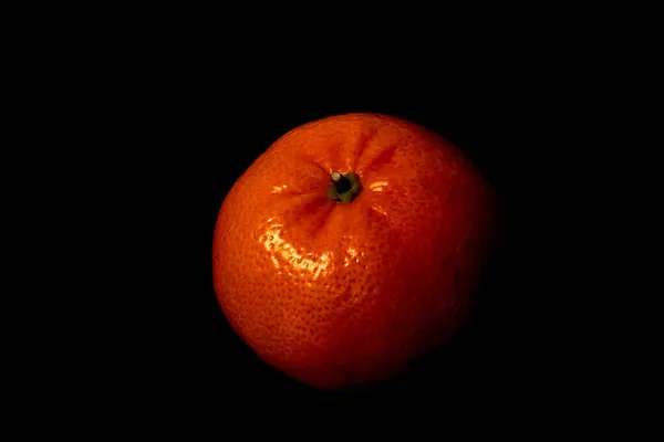 Canlı bir mandalina koyu bir yüzeyde oturur, zengin turuncu rengini ve eşsiz dokusunu vurgular. Parlak cilt ışığı yansıtır, çarpıcı bir kontrast yaratır..