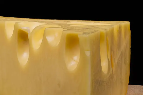 Belirgin deliklerden oluşan bir peynir kamışı, ahşap bir yüzey üzerinde koyu bir arkaplana karşı sergileniyor, desen ve rengini vurguluyor..
