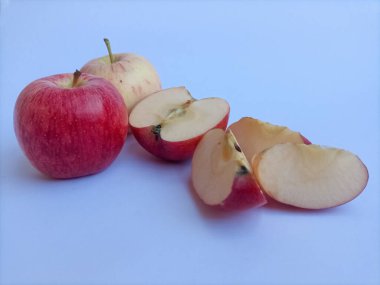 Taze kırmızı ve sarı elma yakın plan, bütün ve dilimlenmiş parçalar, temiz bir mavimsi beyaz arka plan üzerine düzenlenmiş.