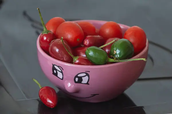 Gülümseyen pembe bir tencere, kiraz domatesli, kırmızı biberli ve yeşil 