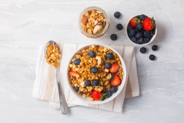 Mısır gevreği kasesinde yulaf, mavi dut ve beyaz arka planda çilek bir peçete üzerinde metal kaşık yulaf küçük kase ve bir kase böğürtlen.