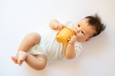 Ağzında fincanla yerde yatan bir bebek.