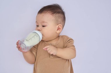 9 aylık çocuk yalan söylüyor ve bir şişe süt tutuyor, uykulu, beyaz arka planda ve doğal ışıkta yatıyor.