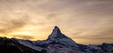 Karla kaplı Matterhorn, güneşin Alpler 'in arkasında battığı ve bulutların altın saat boyunca görülebildiği kış günbatımında.