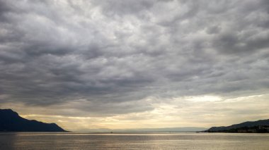 İsviçre 'nin Montreux şehrinden gelen altın saat boyunca gri bulutlu gün batımı, Cenevre Gölü' ne yansıyan güneş ışığı.
