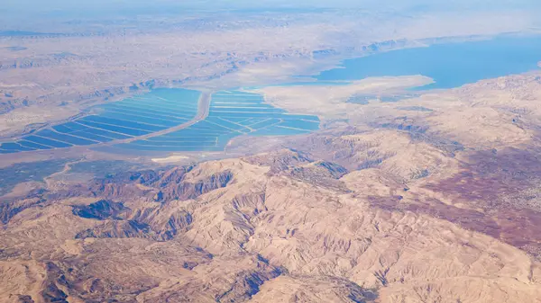 The arid mountains of the Jordanian desert alongside the deep blue of the Dead Sea, seen from above on a sunny day