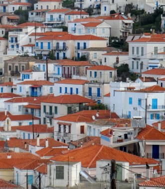 Atina yakınlarındaki Yunanistan 'da bir Akdeniz adasında, birbiri ardına toplanmış turuncu çatıları, mavi pencereleri ve kapıları olan beyaz evler