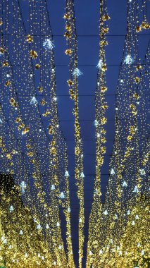 Mavi gökyüzü arka plandayken, sokaktaki Noel ışıkları görüntünün altında kesişiyor.