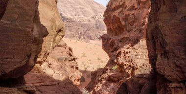 Yüksek uçurumları olan kayalık bir kanyon aşınmış oluşumlar ve ıssız bir bölgede güneşli bir çöl manzarası.