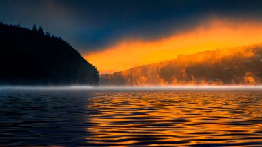 Fransa 'nın güneyindeki La Ravire Gölü üzerindeki gündoğumu manzarası. Güneş ışığı gölden yükselen sisle birlikte sakin suları yansıtıyor. Suya yansıyan ağaç.