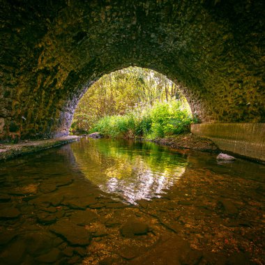 Fransa 'nın güneyinde, akşam üzeri yeşilliğin ortasında taş köprüsü olan bir nehir. Hrault 'taki Arn Nehri' nin manzarası.