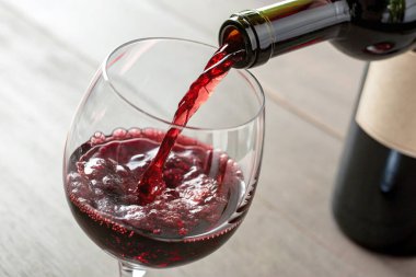 Kırmızı şarabı bir bardağa dolduruyorum. Ahşap arka planda bir şişe var.