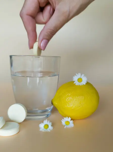 stock image Hand throwing a pill into a glass of water with vitamin C from natural ingredients effervescent tablets and lemons on table