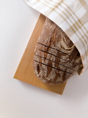 Sliced black bread on a wooden board, covered with a towel. White background, top view clipart