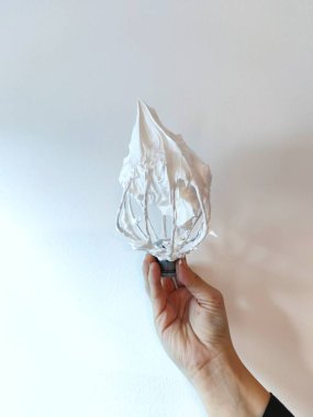 Bir kadının eli çırpılmış kremayla çırpılmış çırpılmış çırpıyı beyaz arka planda tutar. Kurabiye yapma süreci..