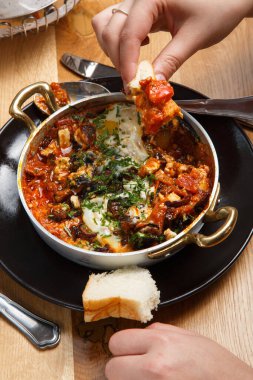 Bir tavada ekmek ile Shakshuka. yemek. Orta Doğu geleneksel çanak. Domates, biber, sebze ve otlar ile kızarmış yumurta. Şakşuka bir tablo. eller üstten görünüm. yakın çekim