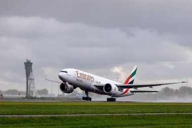 Schiphol, The Netherlands - APRIL 17,  2024. Emirates Boeing 777-F  takes off over the runway on a cloudy rainy day. Emirates is an airline based in Dubai. clipart