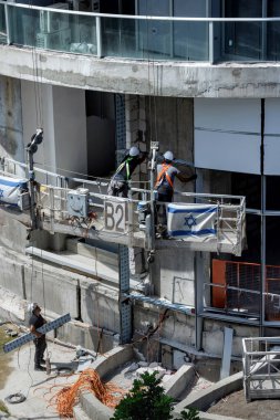 Tel Aviv, Israel - July  30,  2024: Construction workers in hard hats and safety gear handling materials and equipment at a building site. Construction of high-rise buildings in Israel clipart