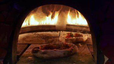 Geleneksel bir fırında pizza pişirmek. Arka plandaki parlak alevler sıcak, otantik bir atmosfer yaratır..