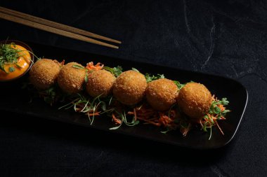 Yengeç eti, deniz ürünleri ve gevrek panko kırıntılarıyla kaplanmış Gouda kroketleri, yanında kremalı sos ve garnitür olarak taze mikroçerez ile altın kahverengiyle servis ediliyor..