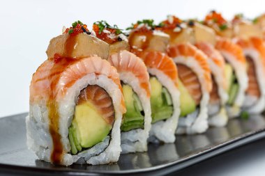 Taze somon, avokado, salatalık ve pirinçle kaplanmış, foie gras, balık yumurtası ve lezzetli sosla süslenmiş lezzetli bir suşi rulosu.